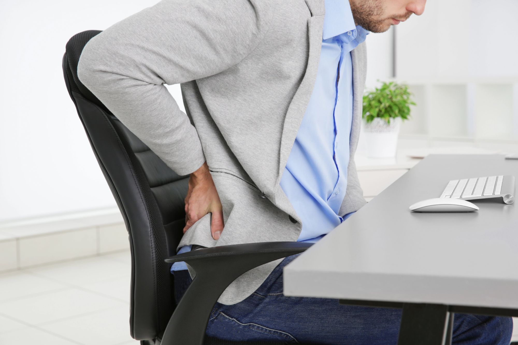 Lower back pain from aggravated pre-existing injury Man in office experiencing severe lower back pain after injury aggravation